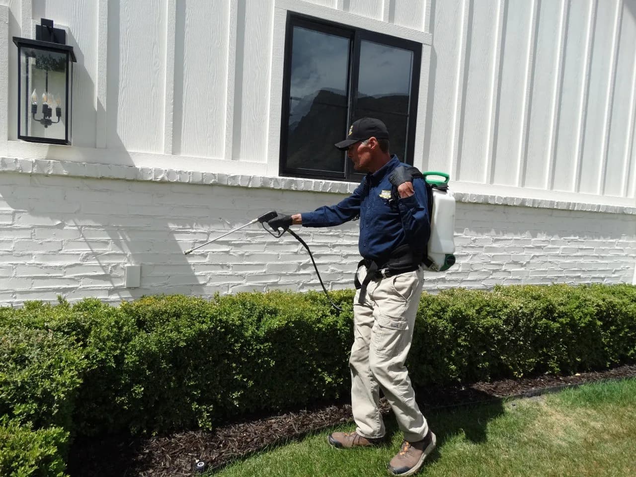 Reynolds technician applying exterior treatment along a home's stone wall